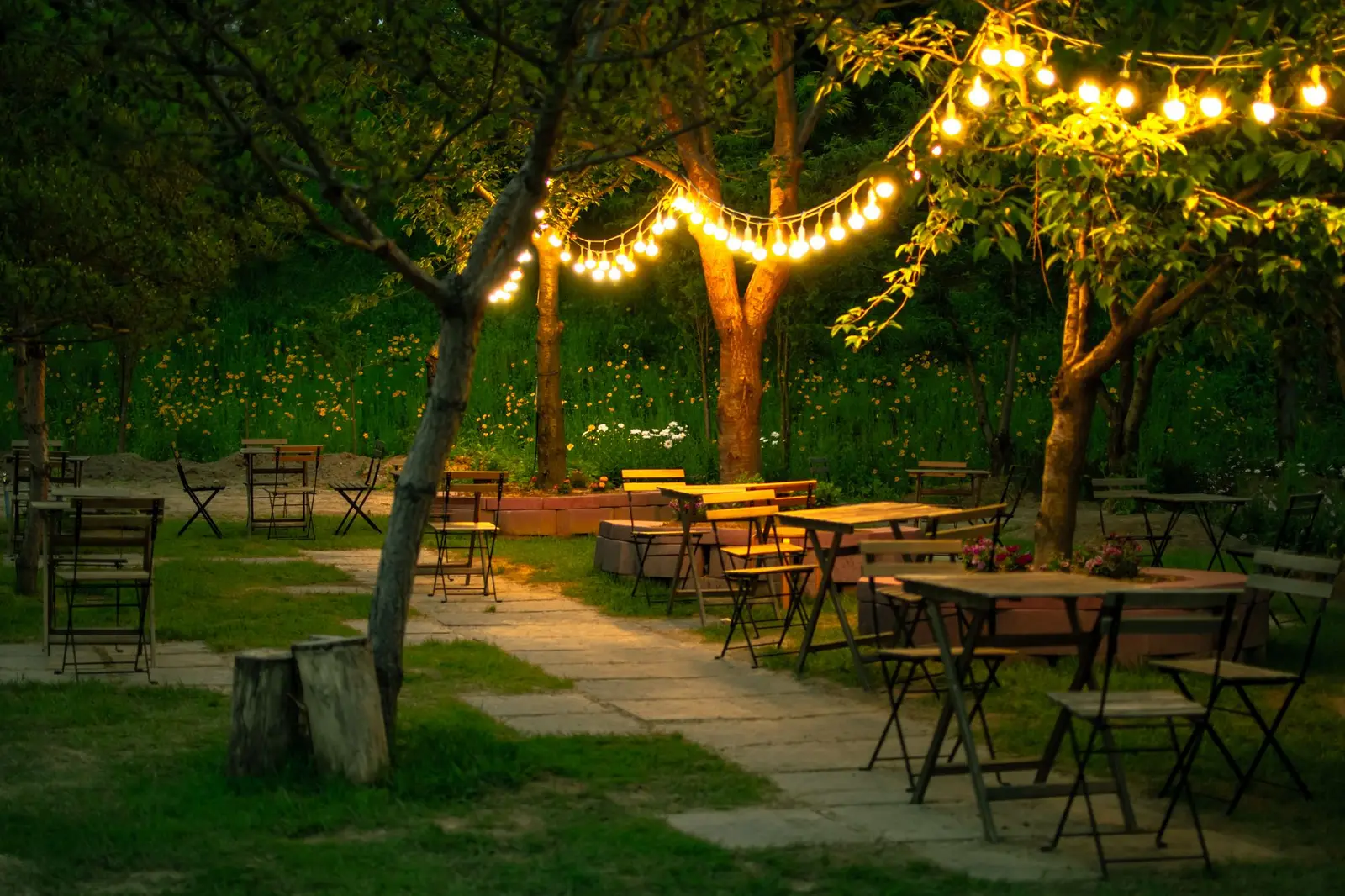 Terrazza del grotto con tavoli in legno e luci tra gli alberi